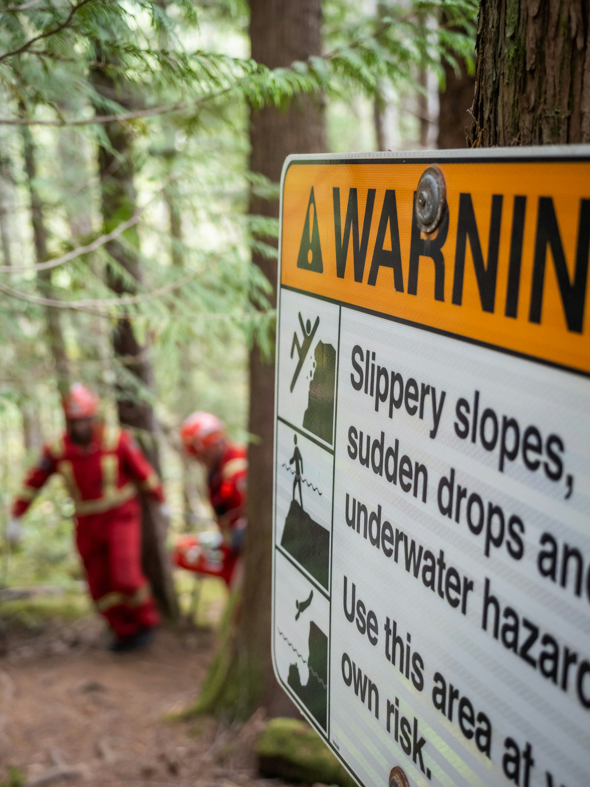 Warning sign in a forest with two people in red gear in the background