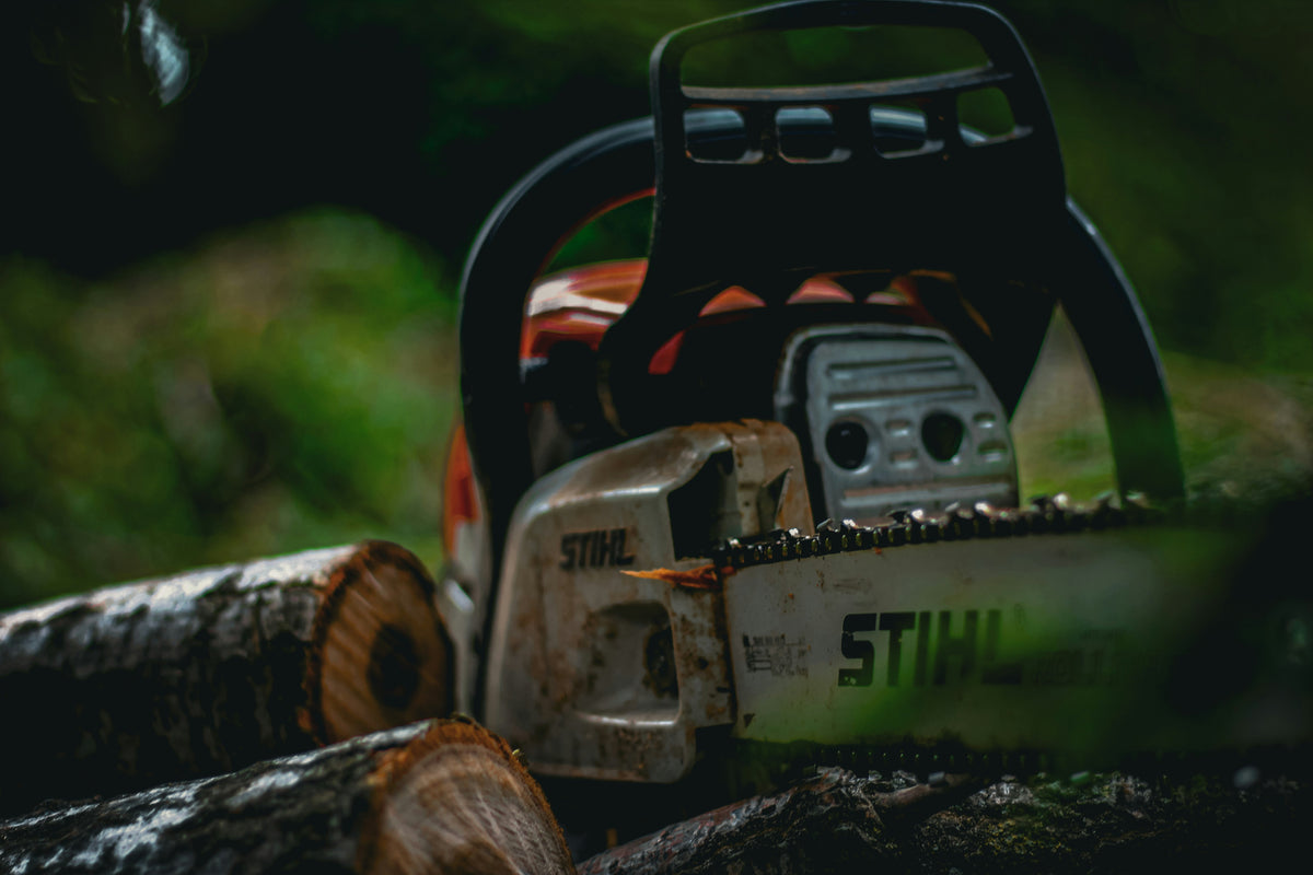 A STIHL chainsaw resting on logs in a forest setting, with blurred green foliage in the background.