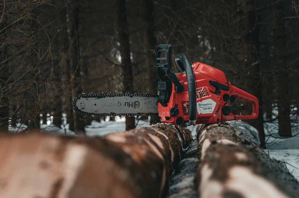Red Husqvarna chainsaw on a log with a forest background
